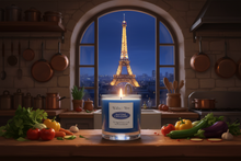 Load image into Gallery viewer, A blue candle in a glass jar sits on a wooden kitchen counter, lit and surrounded by fresh vegetables and cooking utensils. Through the arched window behind it, the Eiffel Tower is visible at night.