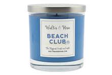 Load image into Gallery viewer, A blue scented candle in a clear glass jar with a brushed silver metal lid. The front features a white rectangular label with the text 'Walter &amp; Rosie' and 'BEACH CLUB'.
